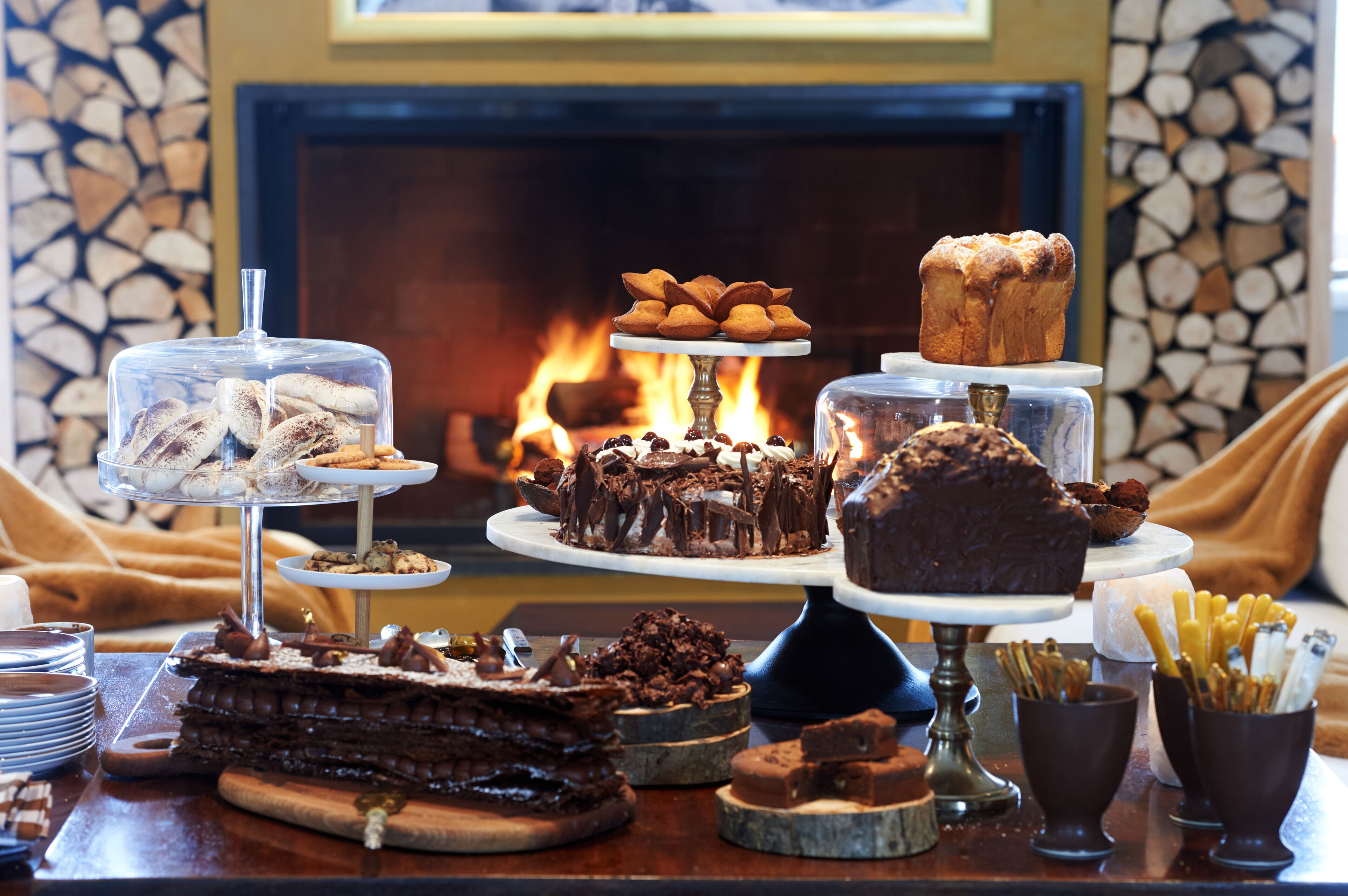 A dessert display with various cakes and pastries in front of a fireplace.