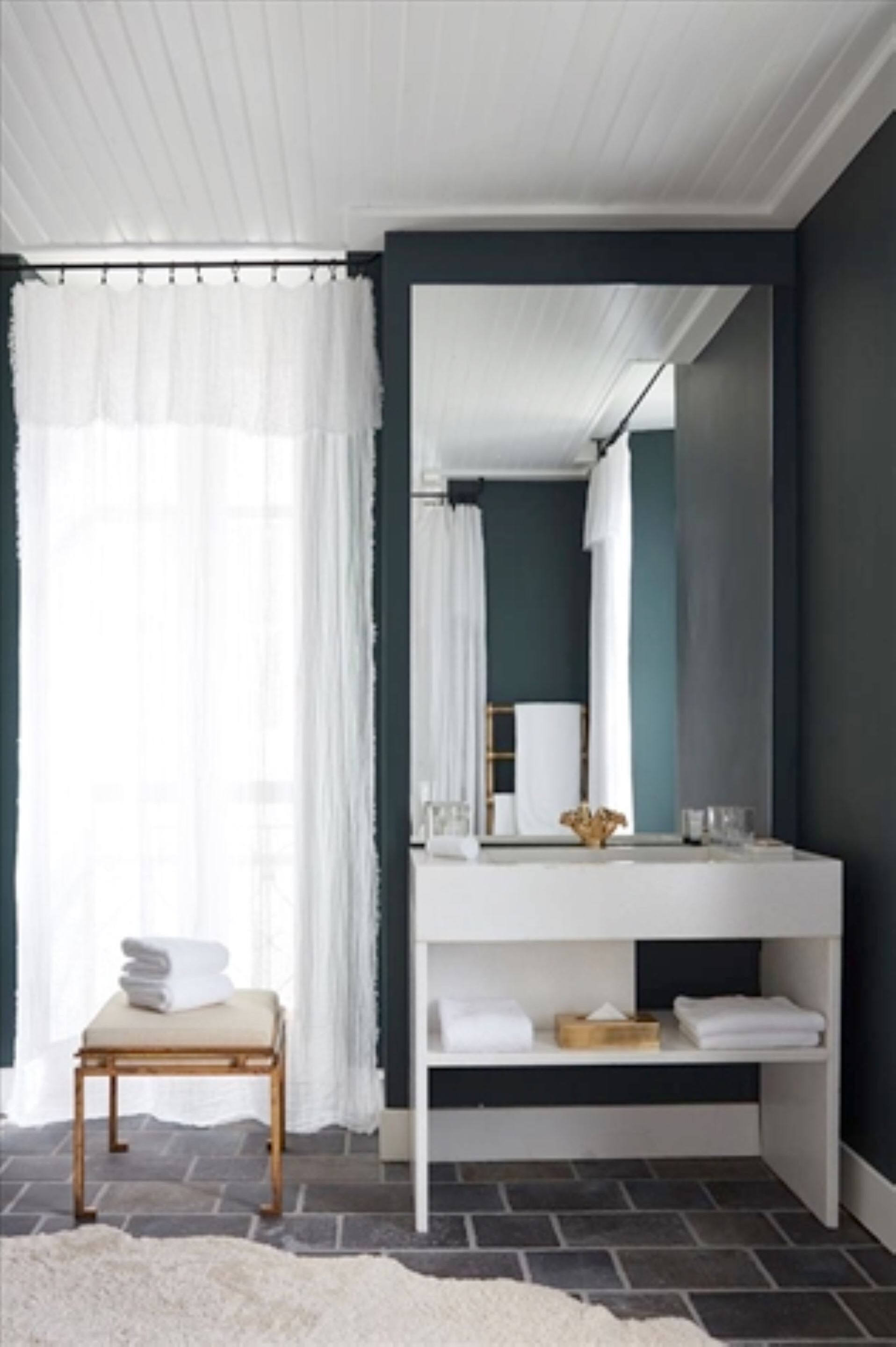 A bathroom with a white vanity, a mirror, and a bench with towels.