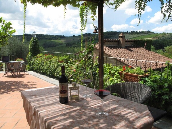 En terrasse med et spisebord, en vinflaske og et glas rødvin.