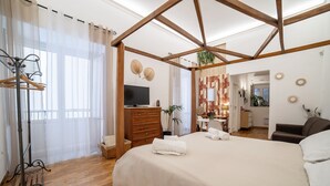 A hotel room with a large bed, wooden floor, a TV, a wooden dresser, and a desk with a chair. - Natoli Apartments - Ina House (Palermo)