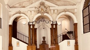 A grand staircase with ornate columns and a decorative ceiling, leading to a central area with a large urn. - Natoli Apartments - Ina House (Palermo)
