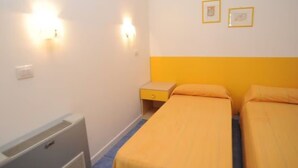 Una stanza con due letti, un termosifone e due luci fissate al muro.