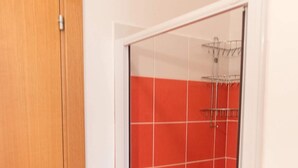 Un bagno con piastrelle rosse e bianche, una porta in legno e una cabina doccia in vetro.