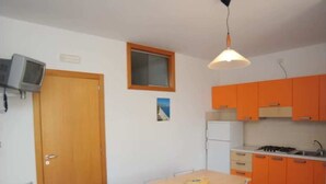 Una cucina compatta con tavolo e sedie, una piccola finestra e un televisore montato a parete.