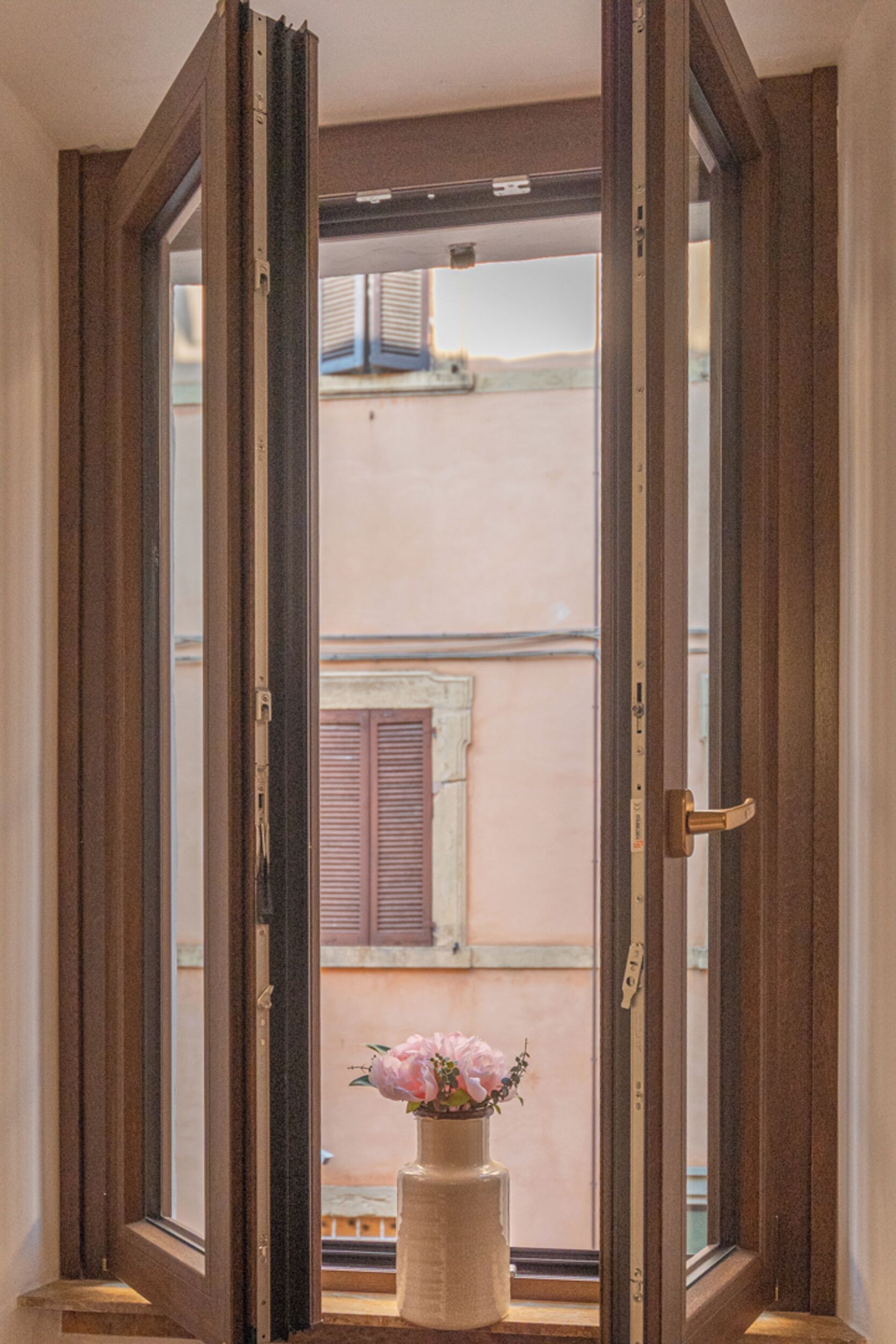 A window with a wooden frame, a brass door handle, and a vase with flowers.