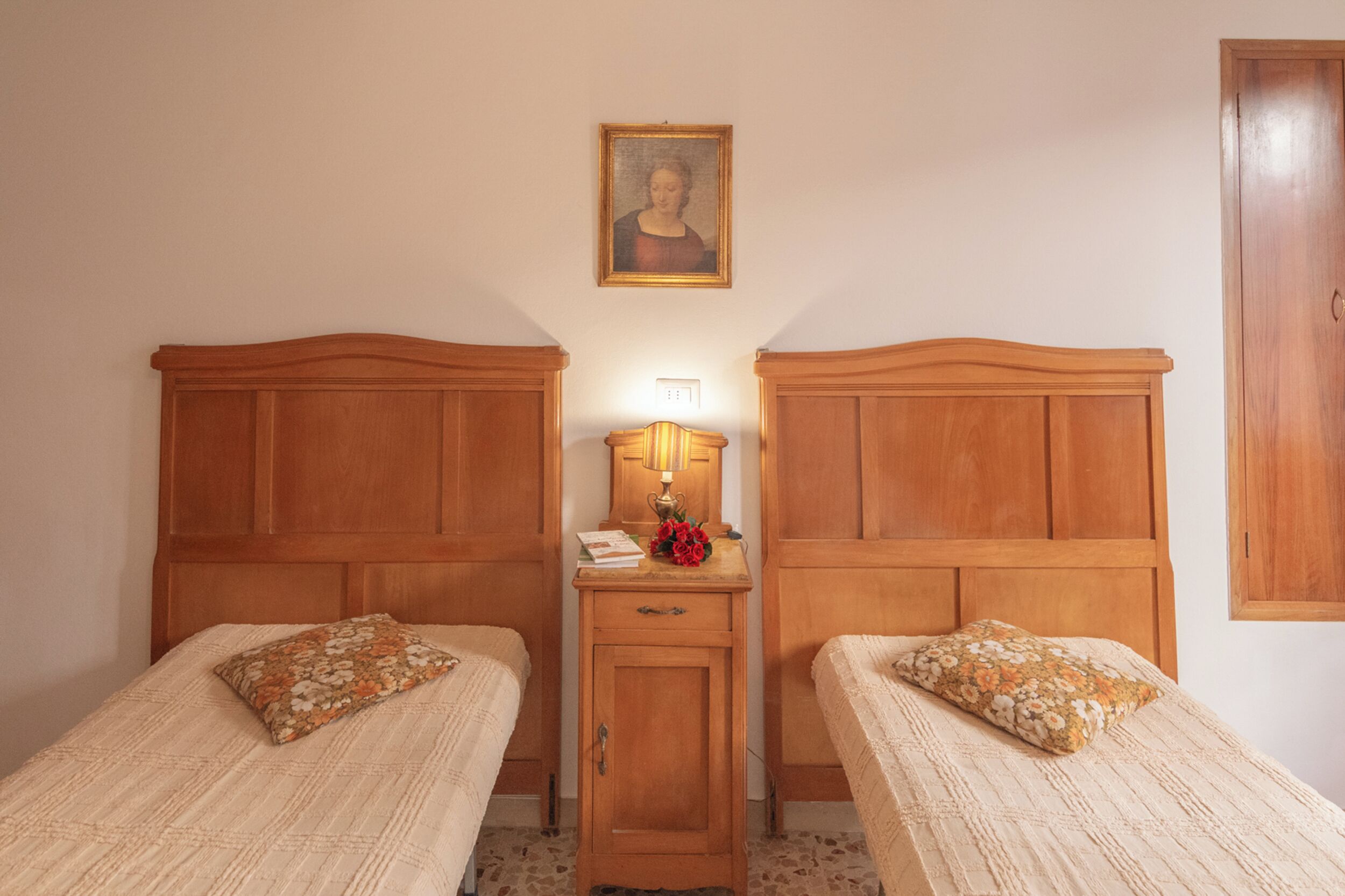 A room with two wooden beds, a nightstand with a lamp, and a framed picture on the wall.