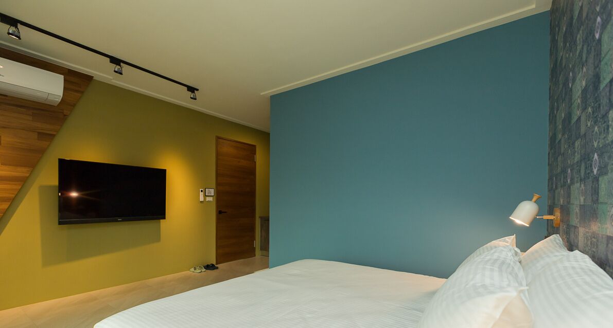 A modern hotel room with a bed, a flat-screen TV mounted on the wall, and a wooden accent wall.