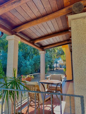 An outdoor patio with wooden beams, a table, chairs, and potted plants. - Comfortable house facing the sea (ogliastra)