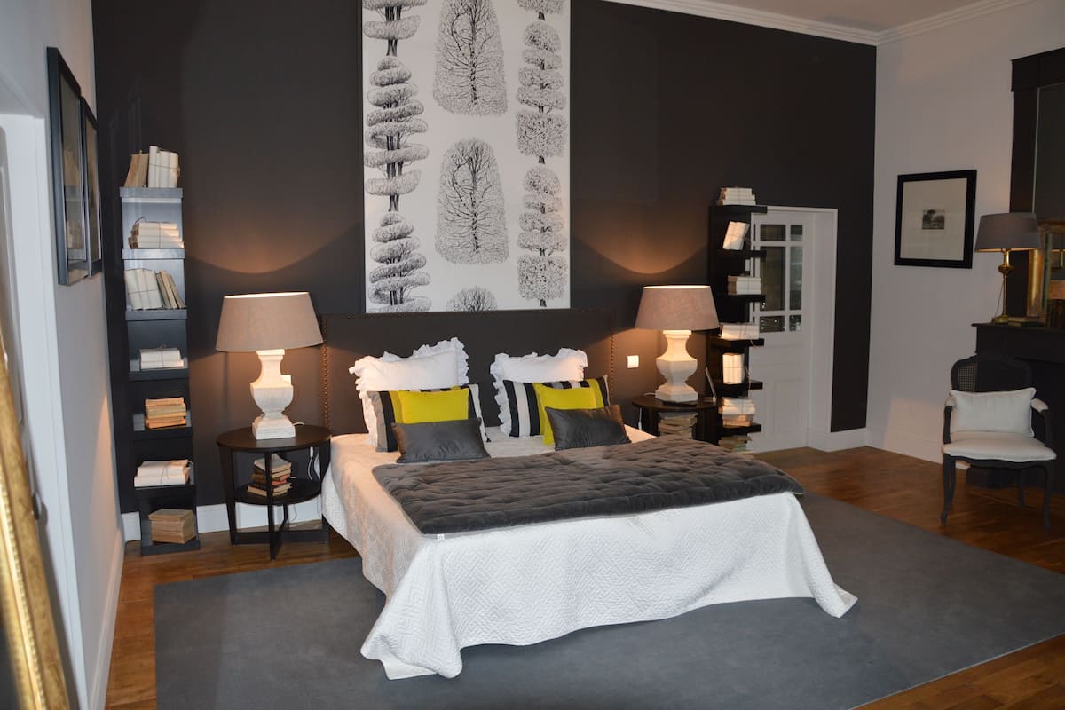 A bedroom with a bed, bedside tables, lamps, a bookshelf, and a door.