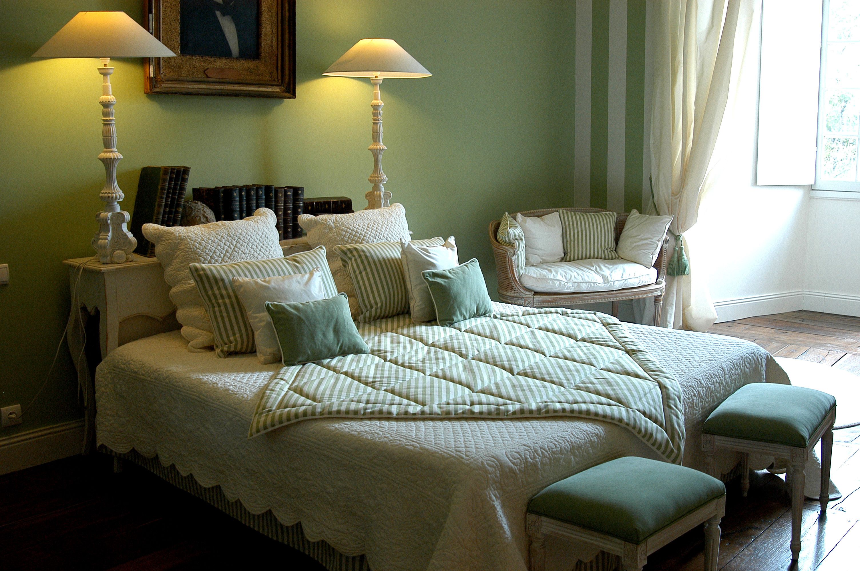 Un dormitorio ordenado con una cama grande, dos mesitas de noche, una silla y una ventana con cortinas.