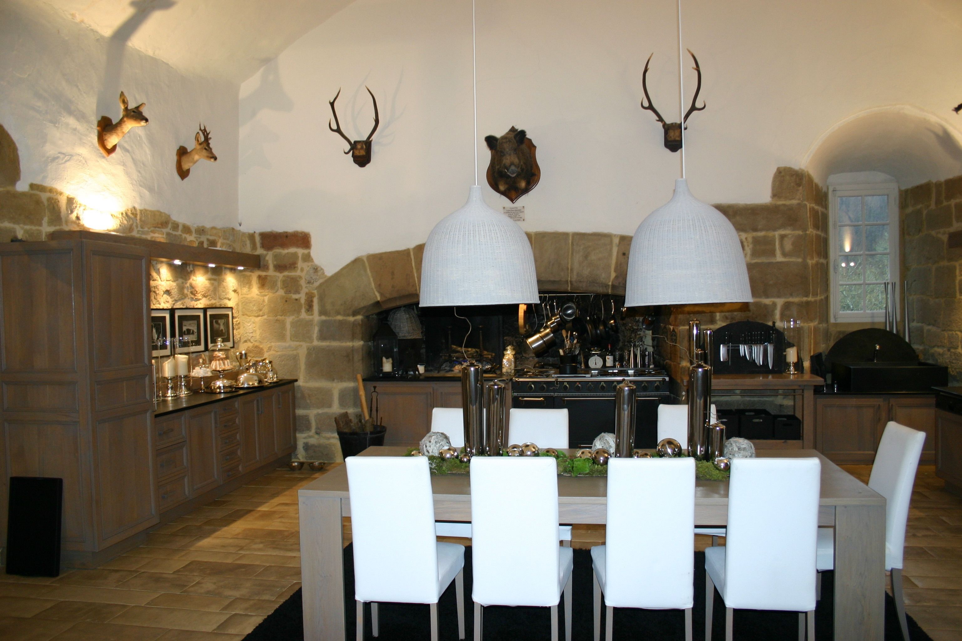 A modern kitchen with stone walls, a wooden dining table, white chairs, and pendant lights.