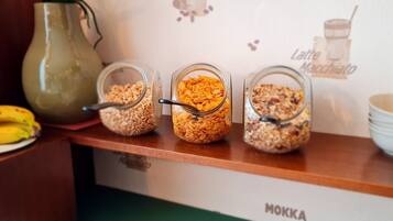 A breakfast bar with three glass containers of cereal, a banana, and a green pitcher.
