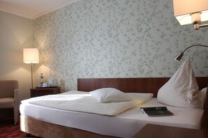 A hotel room with a neatly made bed, a bedside lamp, a chair, and a small table with a water bottle and a cup. - Hotel Garni Försterhof (Kronach)