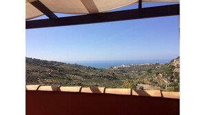 Blick von einer überdachten Terrasse auf eine hügelige Landschaft mit einer fernen Küstenlinie.
