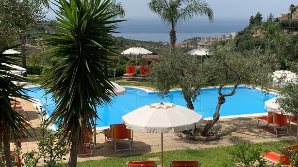Ein Poolbereich mit freiem Blick auf das Meer, umgeben von Palmen und Sitzgelegenheiten im Freien.