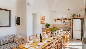 Ein Essbereich mit einem langen Holztisch, der für eine Mahlzeit gedeckt ist, einer Küche im Hintergrund und einem gestreiften Sofa im Vordergrund.