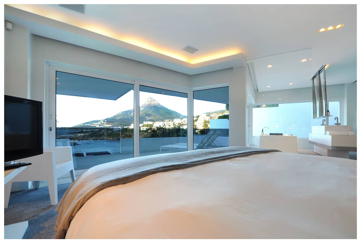 A modern hotel room with a large bed, a TV, and a balcony with a view of a mountain and cityscape.