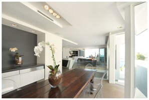 A modern kitchen with a wooden dining table, clear chairs, and a vase with white flowers.