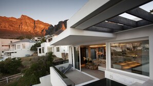 A modern house with a glass facade, outdoor seating area, and a view of a mountain. - Ebb Tide (Cape Town)