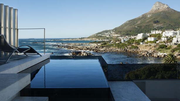 A modern outdoor pool area with a view of the sea and a mountain in the background. - Ebb Tide (Cape Town)