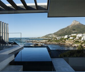 A modern outdoor pool area with a view of the sea and a mountain in the background. - Ebb Tide (Cape Town)