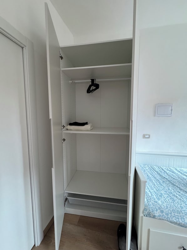 A room with a wardrobe, a bed with patterned bedding, and a shoe rack.