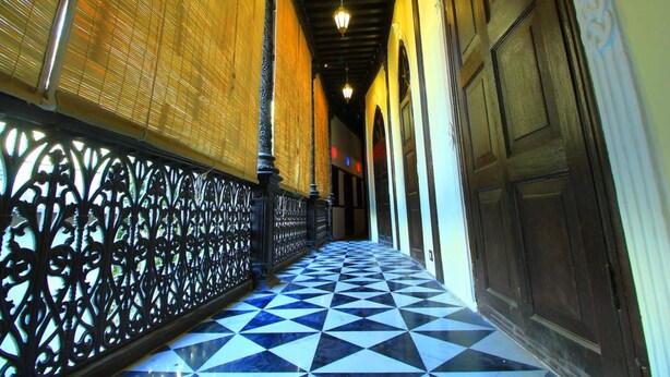 Un pasillo con suelo a cuadros blanco y negro, barandales de metal negro ornamentados y puertas de madera.