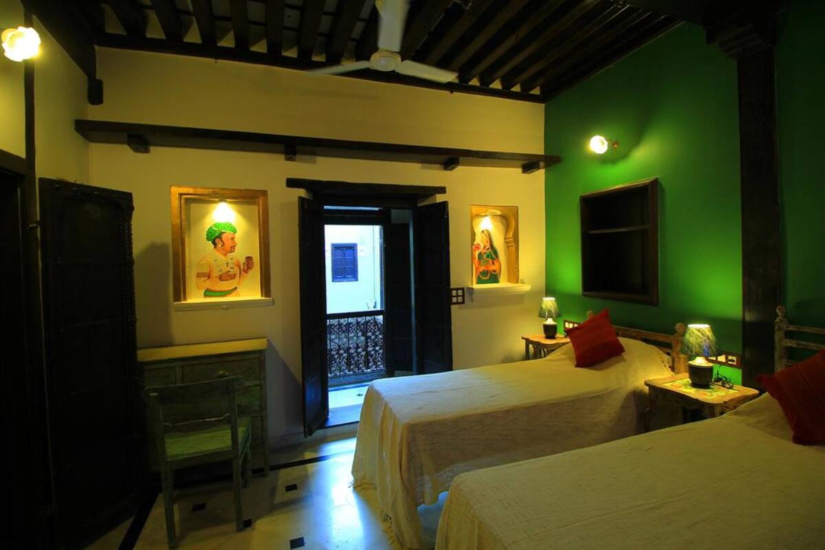 A room with two beds, a desk, and a chair. There is a door leading to an outdoor area.