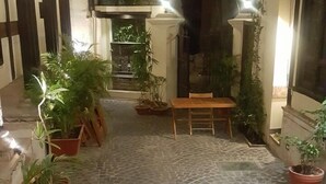 Un patio con suelo de baldosas, plantas en macetas y un banco de madera.