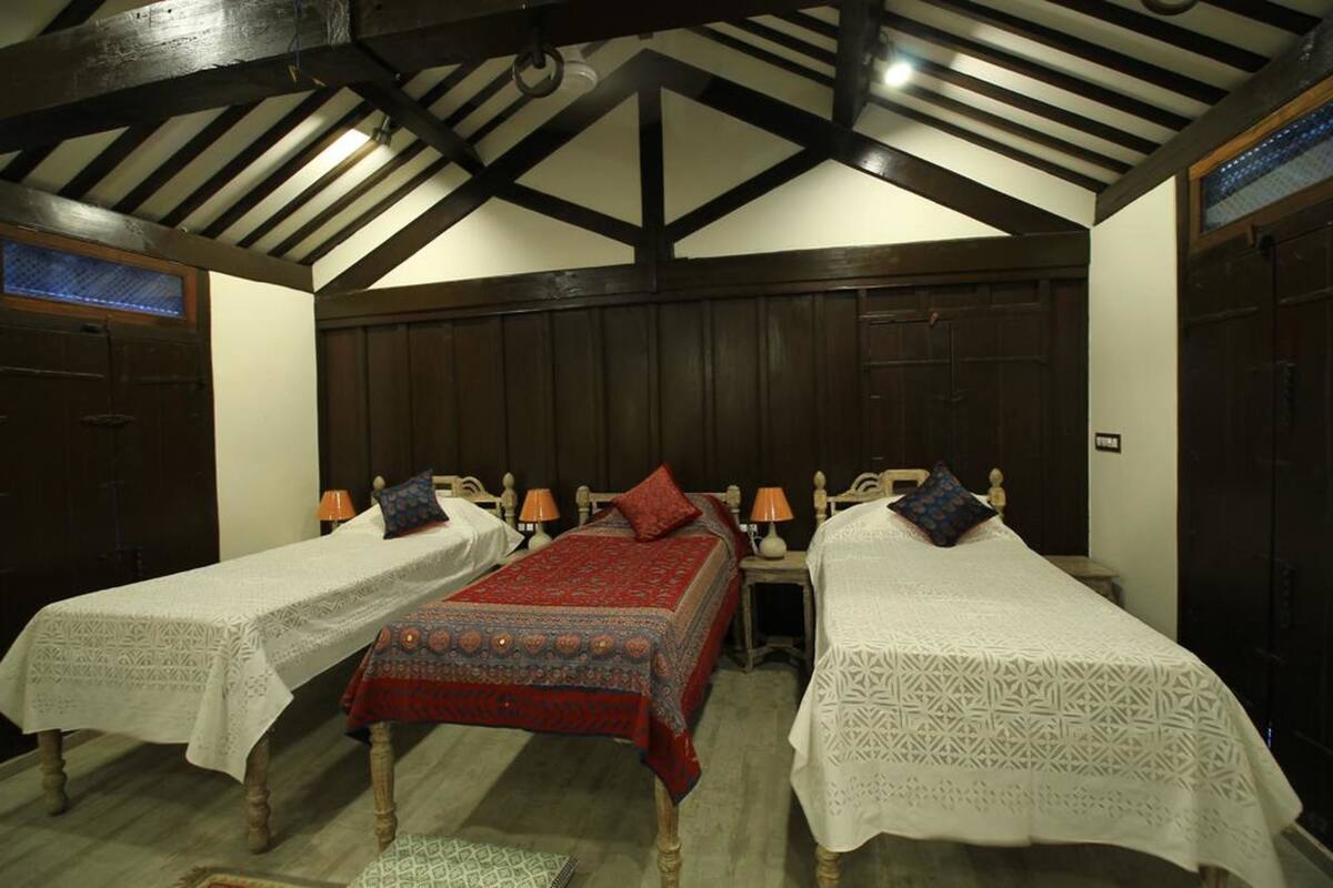 A room with two single beds, each with a white lace bedspread and a red patterned bedspread. The room has wooden beams on the ceiling and dark wooden walls.