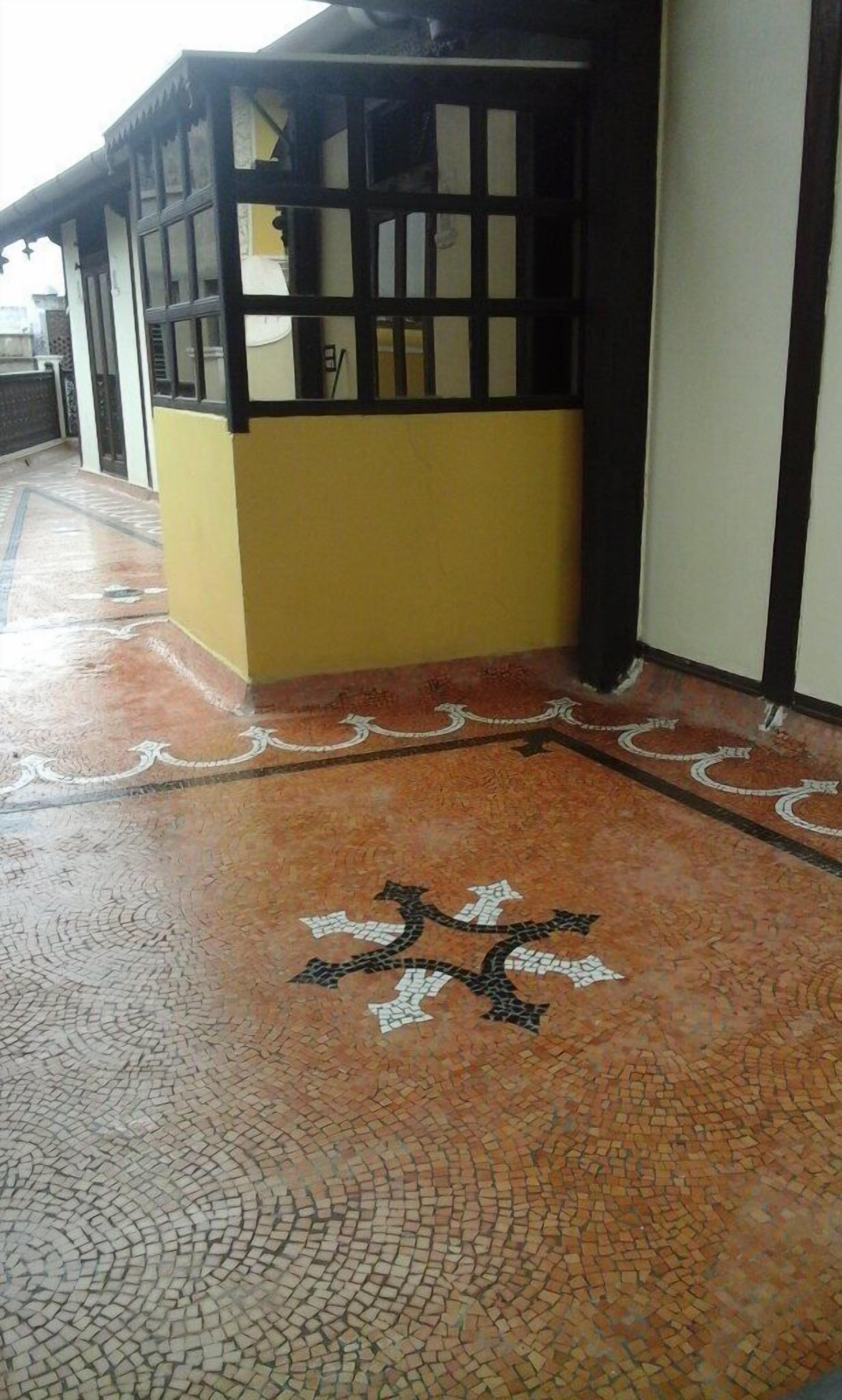 Ein Gebäude mit einer gelb-schwarz gestreiften Fassade, einem Fliesenboden mit geometrischem Muster und einer teilweise sichtbaren Tür.