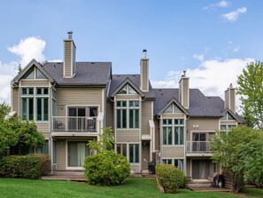 Een woonhuis met twee verdiepingen, een balkon op de tweede etage, en een schoorsteen op elk dak, met een verzorgd gazon.