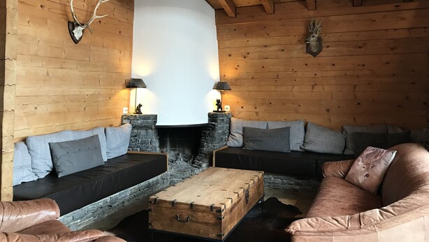 Interior acogedor de una cabaña de madera con chimenea de piedra, sofás de cuero y adornos de asta de ciervo.