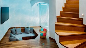 Un interior moderno con una escalera de madera, una zona de estar integrada y una puerta de cristal que da a otra habitación.