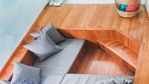 Un baño moderno con cabina de ducha de vidrio, un banco de madera con cojines y una cesta pequeña con toallas.