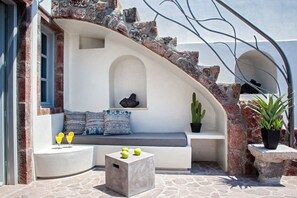 Un espace extérieur ensoleillé, aménagé avec des sièges, un banc en pierre, une petite table avec des boissons et des plantes en pot.