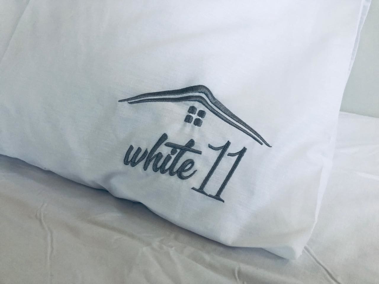 Almofada com um desenho de casa e a inscrição "white 11" bordada.