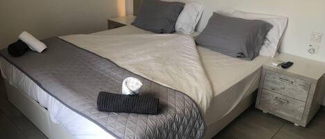A neatly made bed with a quilted cover, pillows, and a folded towel. There is a nightstand with a remote control and a power outlet.