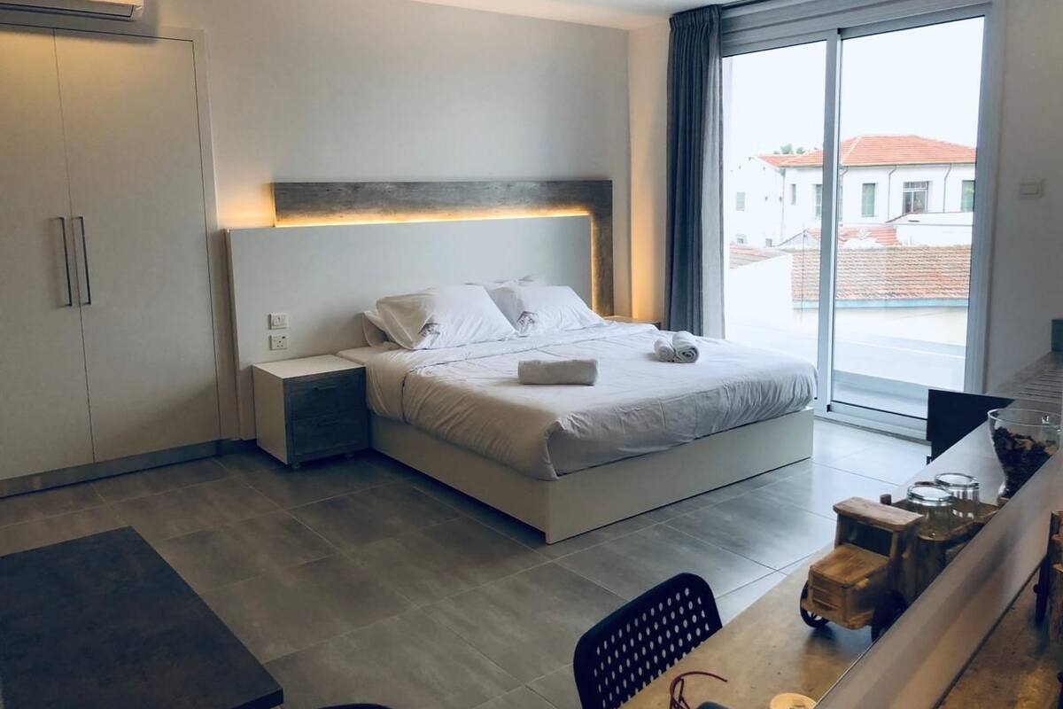 Quarto de hotel moderno com uma cama grande, mesas de cabeceira, uma escrivaninha e vista para o exterior.