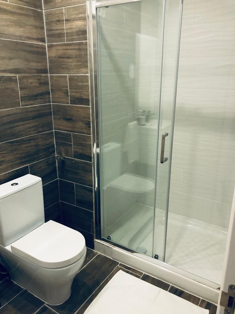 A bathroom with a glass-enclosed shower, a white toilet, and dark wood-patterned tiles.