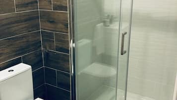 A bathroom with a glass-enclosed shower, a white toilet, and dark wood-patterned tiles.