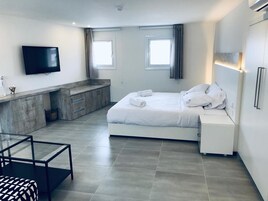 Un dormitorio moderno con cama, mesitas de noche, televisor y un pequeño rincón de descanso.