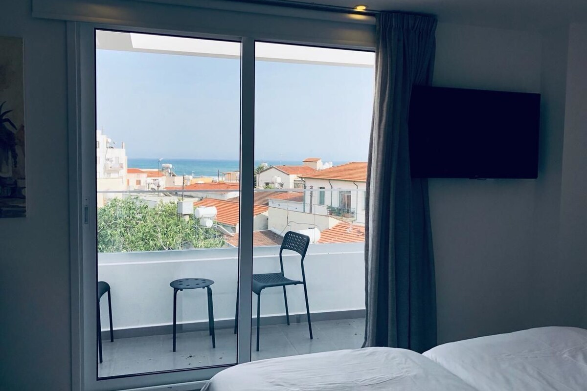 A hotel room with a balcony, a bed, a TV, and two chairs.