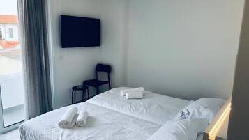 Habitación de hotel con una cama, un televisor de pantalla plana montado en la pared, una silla y un ventanal con cortinas.