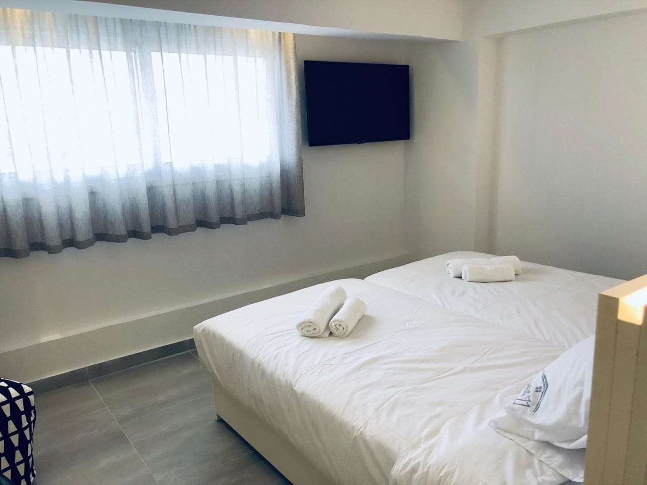 A hotel room with a bed, a TV mounted on the wall, and a window with curtains.