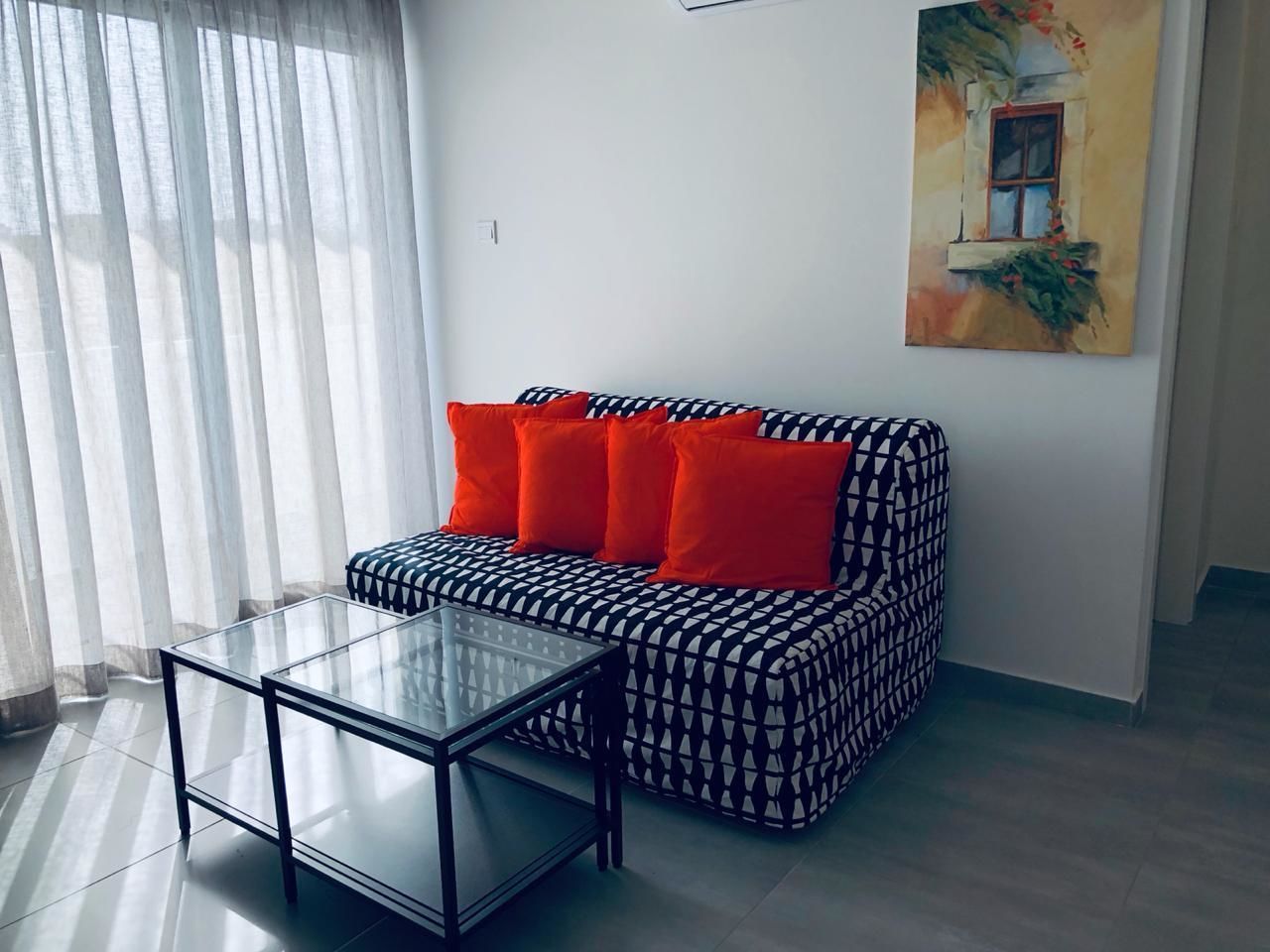 Ein Wohnzimmer mit einem gemusterten Sofa, einem Glastisch und einem Bild an der Wand.