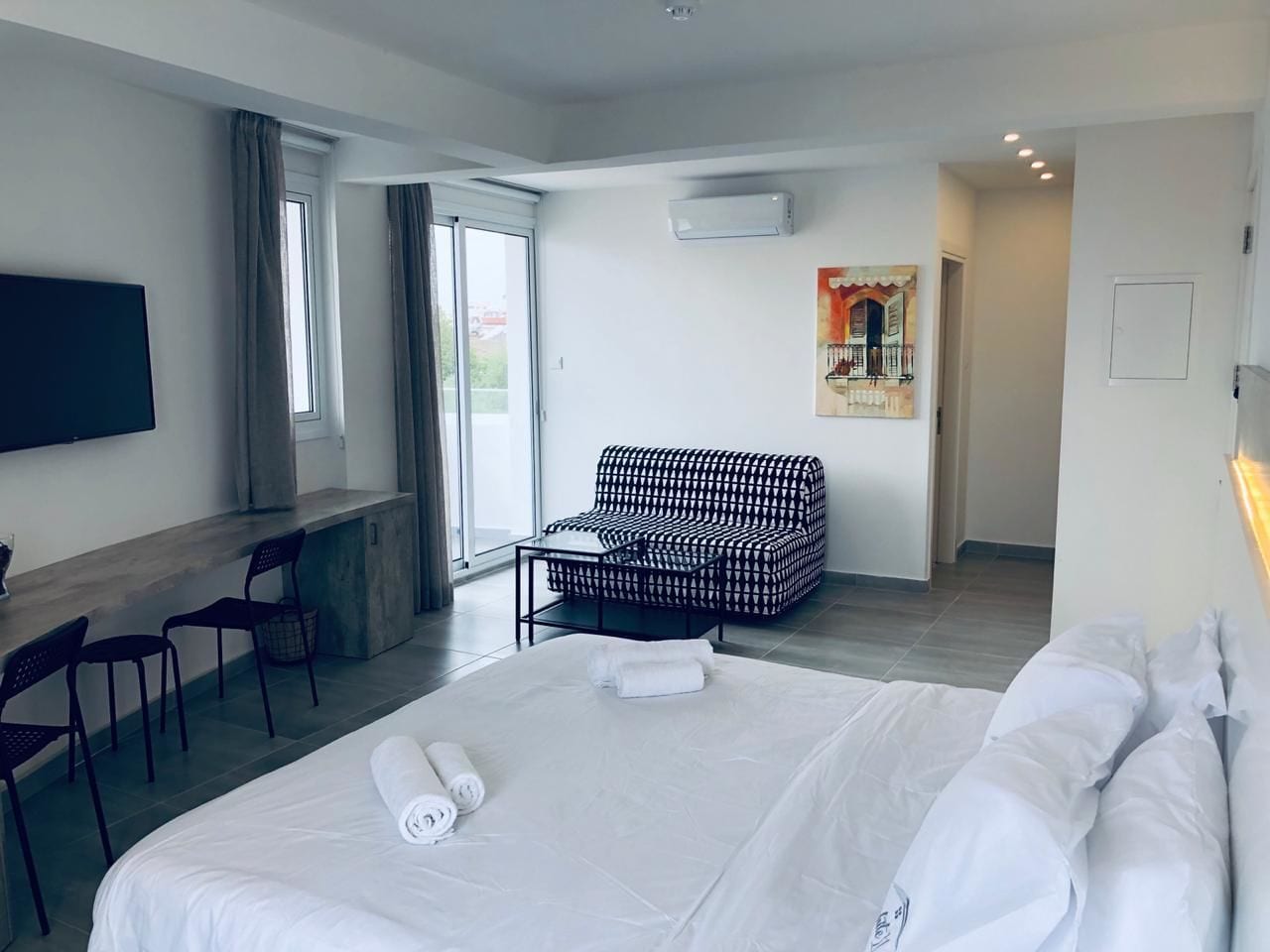 A hotel room with a large bed, a sofa, a desk, and a TV.