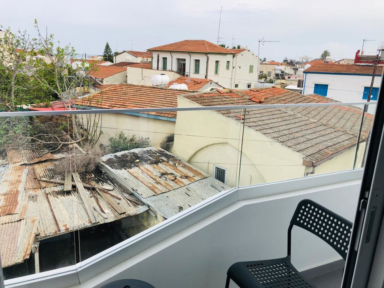 Ein Balkon mit Blick auf angrenzende Gebäude, darunter ein Gebäude mit rotem Ziegeldach und ein weiteres mit weißer Fassade.