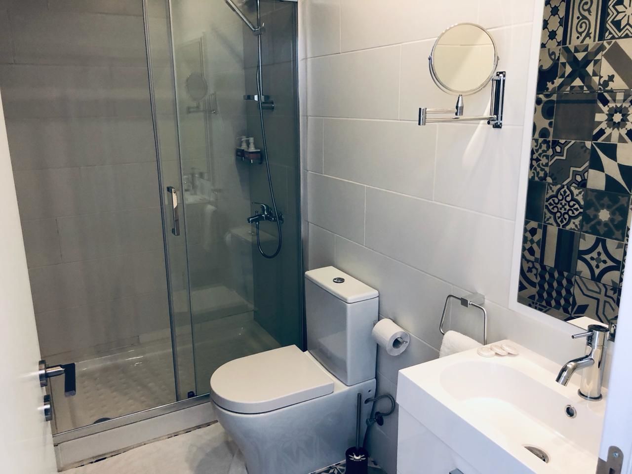 A modern bathroom with a glass-enclosed shower, a toilet, and a sink with a mirror.