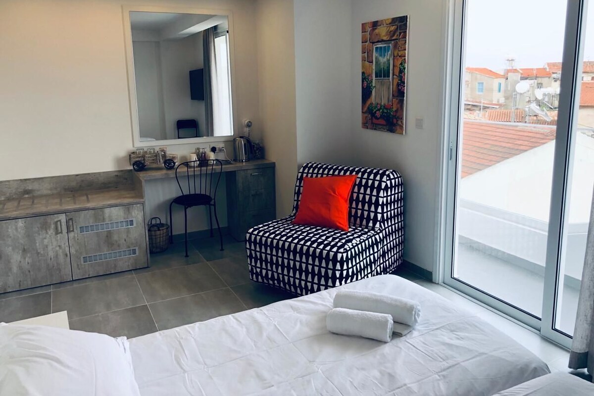 A hotel room with a bed, a chair, a desk, a mirror, and a window.